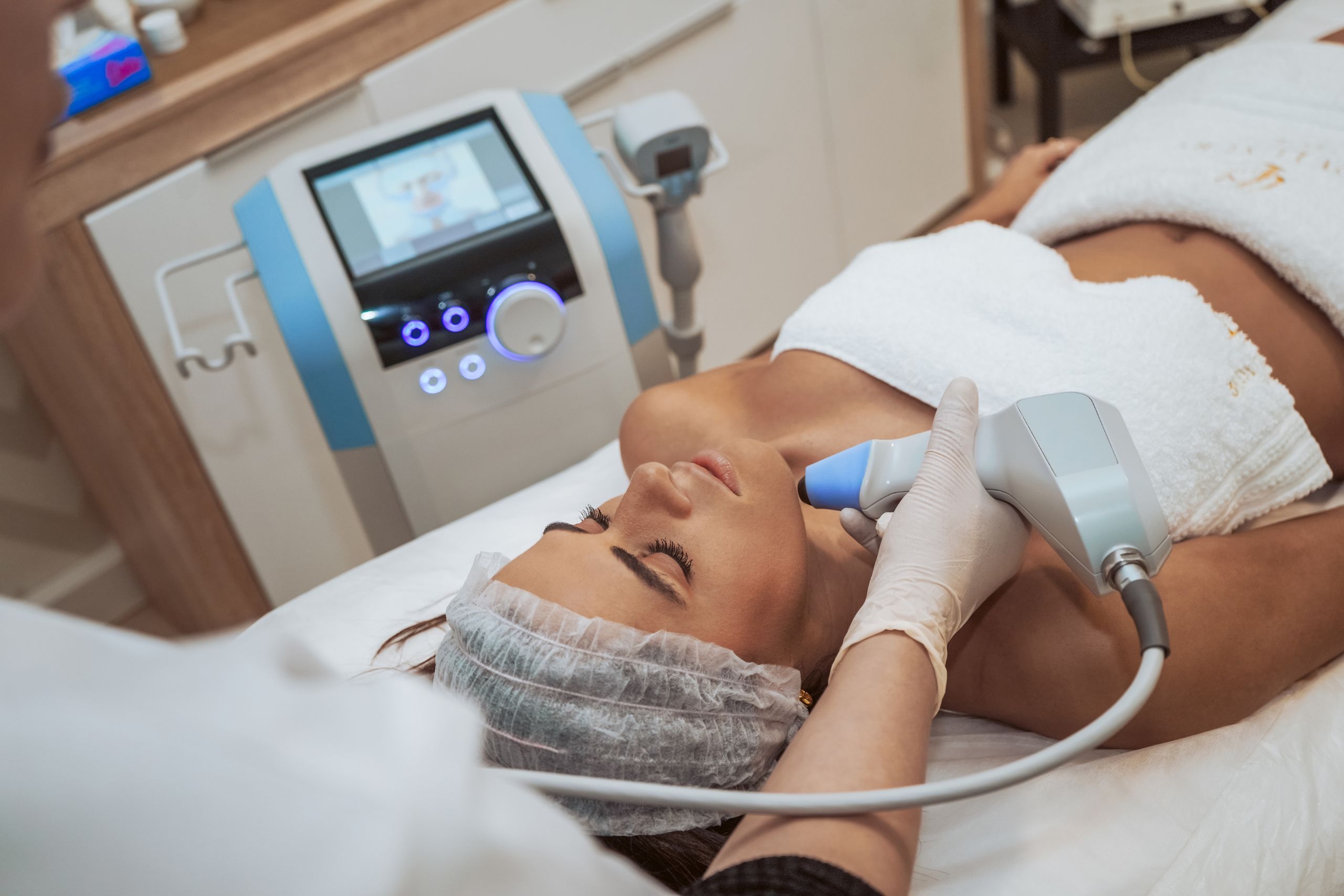 A close-up image of a young woman laying on an examination table in a doctors office, appearing to be receiving an aesthetic treatment